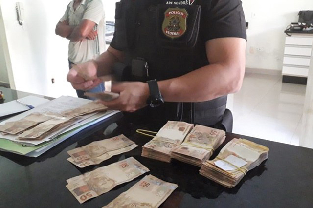 Policial federal inspeciona dinheiro apreendido em operação (Foto: PF-RO/Divulgação)