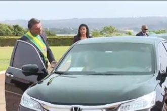 Presidente Jair Bolsonaro gesticula para Michelle, que está dentro do carro (Foto: TV Brasil/Reprodução)