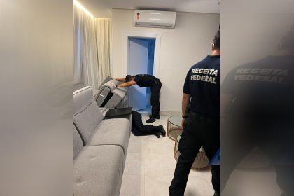 Agentes da Receita vasculham sofá em casa de suspeito (Foto: PF-AM/Divulgação)