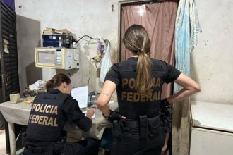 Policiais da PF analisam documentos e computador na casa do suspeito (Foto: Divulgação/PF)