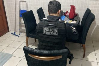 Agente federal inspeciona material em casa de suspeito (Foto: PF/Divulgação)