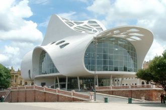 Cobertura curva de concreto branco seria marca de Oscar Niemeyer se tivesse projetado o teatro Amazonas (Imagem: Firefly/Gemini Flash/Divulgação)